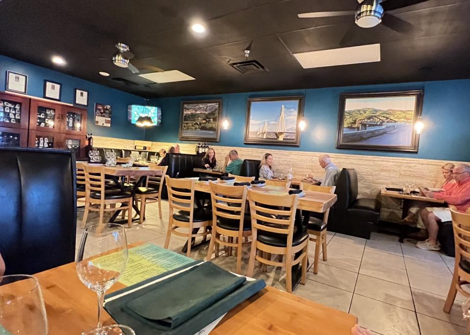 At The Grove Cucina & Wine in Hobe Sound, the decor is comfortable with dark teal walls, light rustic paneling and large framed art on the walls. The tables and chairs are wood tone with black leather seats and booths.