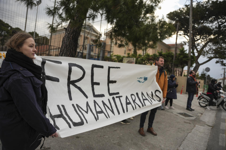 Supporters of the 24 aid workers and volunteers of 24 aid workers and volunteers accused of participating in migrant rescue operations hold up a banner outside the court in Mytilene, on the northeastern Aegean island of Lesbos, Greece, Tuesday, Jan. 10, 2023. A Greek court was set to hear a smuggling-related criminal case Tuesday against a group of 24 aid workers and volunteers. The defendants deny all charges and say all they did was help rescue endangered people. International human rights groups have widely criticized the prosecution. (AP Photo/Panagiotis Balaskas)