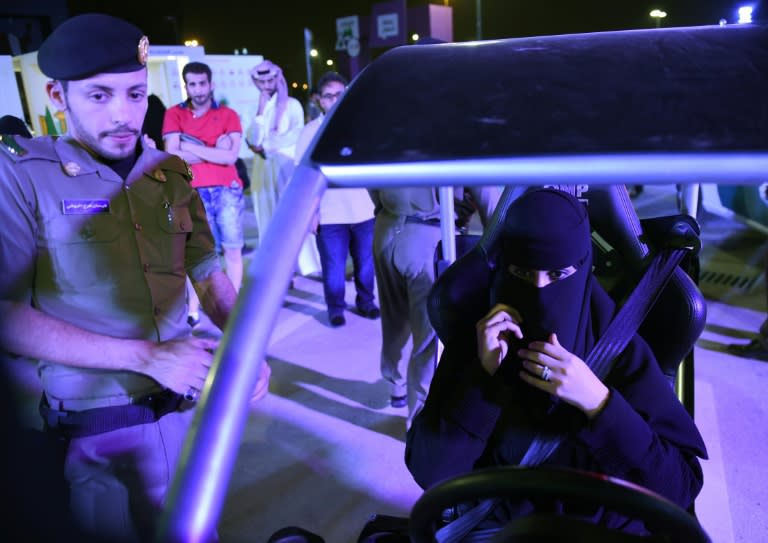 A Saudi police officer stands near a woman preparing to use an electronic driving simulator during a driving workshop for women in the Saudi capital Riyadh