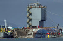 Workers try to raise the sunken Sewol ferry between two barges during the salvage operation in waters off Jindo, South Korea, Thursday, March 23, 2017. The 6,800-ton South Korean ferry emerged from the water on Thursday, nearly three years after it capsized and sank into violent seas off the country's southwestern coast, an emotional moment for the country that continues to search for closure to one of its deadliest disasters ever. (Lee Jin-wook/Yonhap via AP)