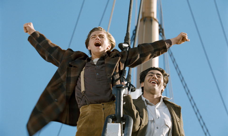 A smiling young man holding his hands up on a ship