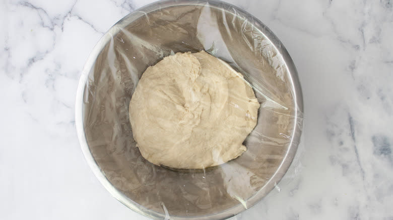 plastic wrap covering dough in bowl