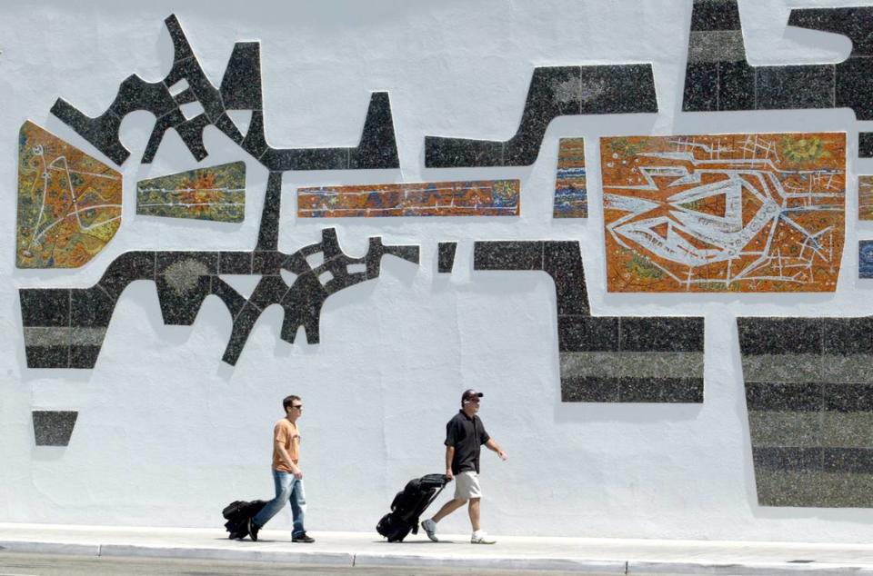 A pair of outgoing travelers walk past the large mural outside the terminal building at the Fresno Yosemite International Airport on their way to catch a flight.