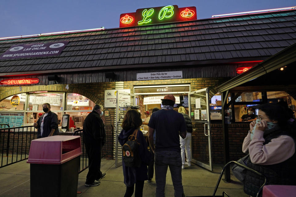 A woman adjusts her mask, right, as people wait in line to order pizza at L&B Spumoni Gardens in the Gravesend neighborhood of Brooklyn, and near the Bensonhurst neighborhood, Sunday, Oct. 4, 2020, in New York. The well-known Italian restaurant specializing in pizza and Italian ices attracts people from all over Brooklyn and is in a Zip Code that is experiencing a rise in coronavirus cases. L&B's indoor dining is currently closed, but if new restrictions proposed by New York's mayor go into place this week, the restaurant's outdoor seating area may have to be shut down. (AP Photo/Kathy Willens)