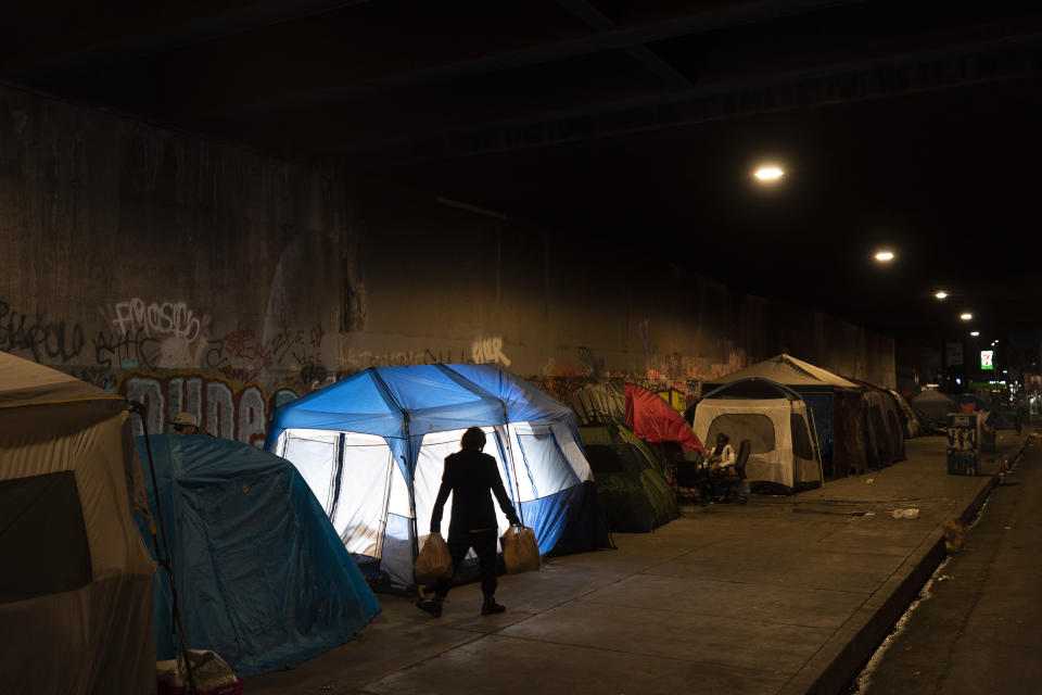 Archivo - Un hombre camina junto a un campamento de indigentes instalado debajo de un puente en Los Ángeles, el 9 de febrero de 2023. La tienda de campaña azul fue iluminada desde el interior mediante un flash externo, (AP Foto/Jae C. Hong, Archivo)