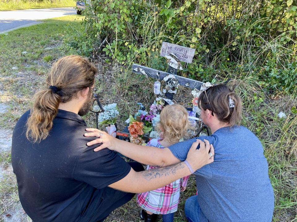 Heath Mabey, 19, his cousin, Lilliana Cassidy, 2, and his aunt Kendra Cassidy, have a moment of silence in front of his father Michael Berry's roadside memorial in Osteen. Berry was kneeling at his friend's memorial when he was killed by a hit-and-run driver.