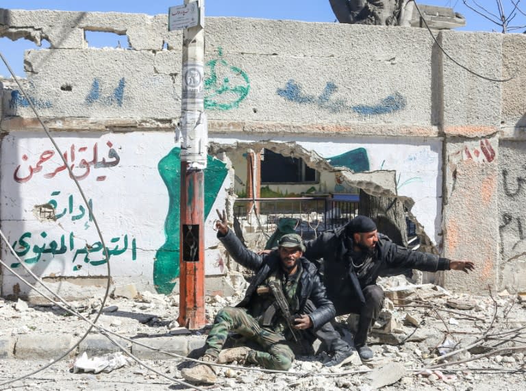 Syrian pro-government fighters pose in front of a wall bearing the legend "Faylaq al-Rahman, department of morale", in the town of Jisreen in Eastern Ghouta, on March 17, 2018