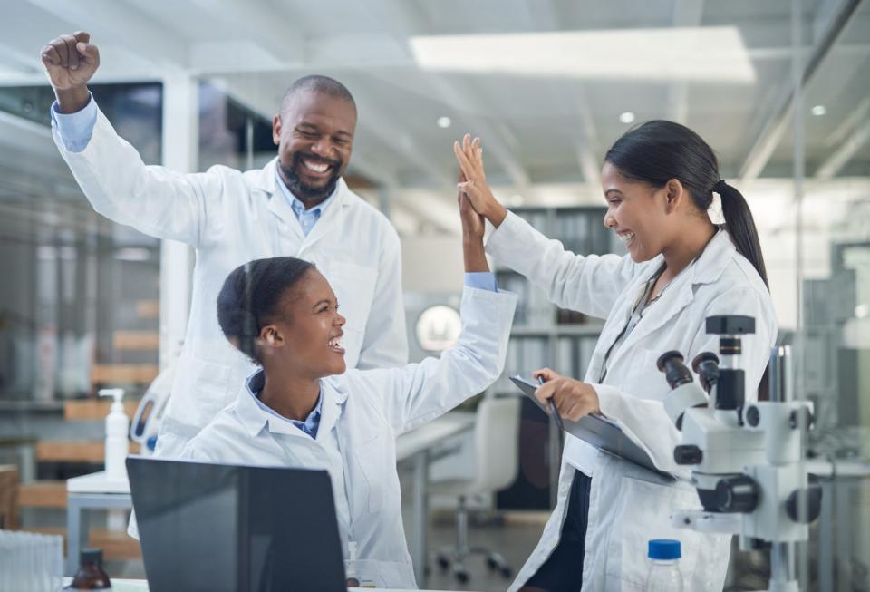 Three smiling researchers in a lab give each other high fives.