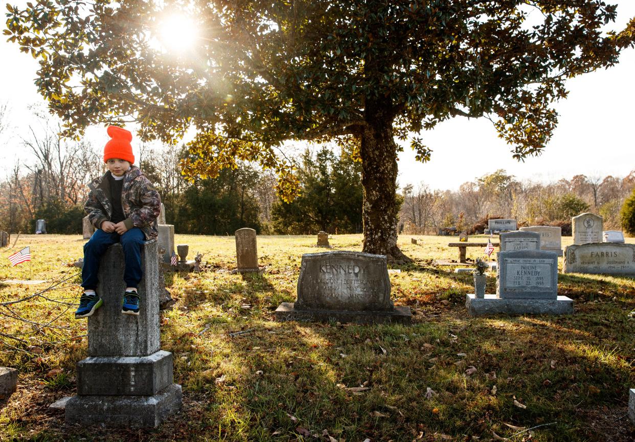 The eighth generation of a Maury County farming family, Samuel Kennedy IV sits on his great great grandmother's headstone in a family cemetery located on the family's 210-year-old Kettle Mills Farm in Columbia, Tenn. on Nov. 18, 2022.