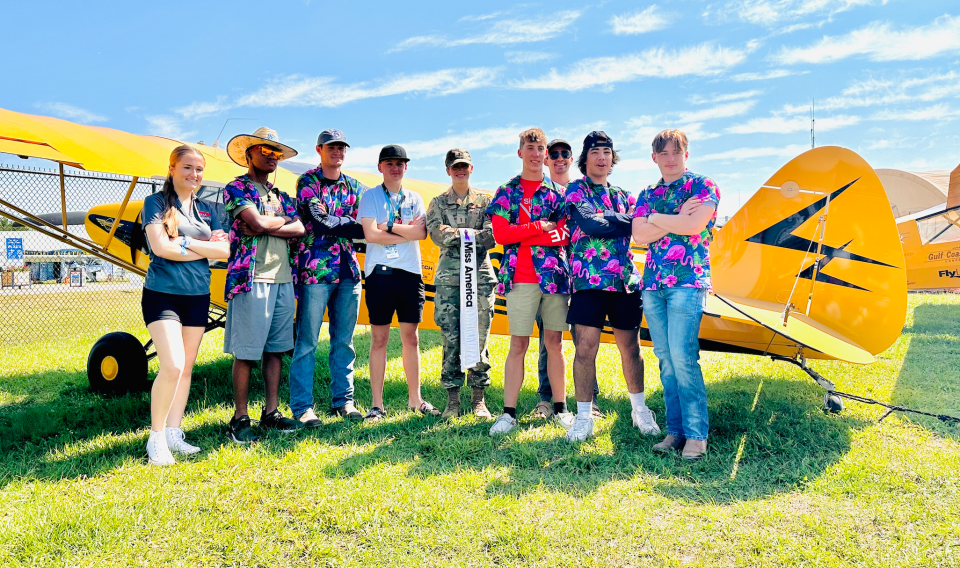 Lakeland Aero Club members, dressed in Hawaiian shirts and known as "The Cavalry" during Sun 'n Fun this year, gather in front of a Piper PA-11 plane to take a picture with 2024 Miss America Madison Marsh, center. Marsh is an active second lieutenant in the U.S. Air Force and a civilian pilot.