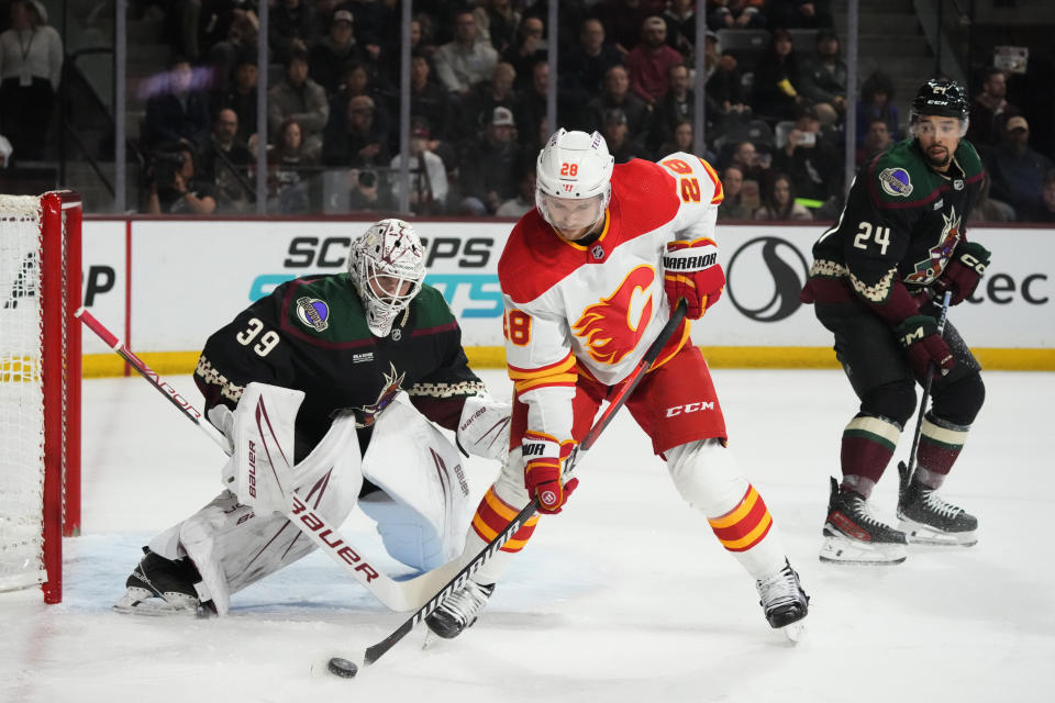 Calgary Flames center Elias Lindholm (28) skates with the puck in front of Arizona Coyotes goaltender Connor Ingram (39) and Coyotes defenseman Matt Dumba (24) during the second period of an NHL hockey game Thursday, Jan. 11, 2024, in Tempe, Ariz. (AP Photo/Ross D. Franklin)