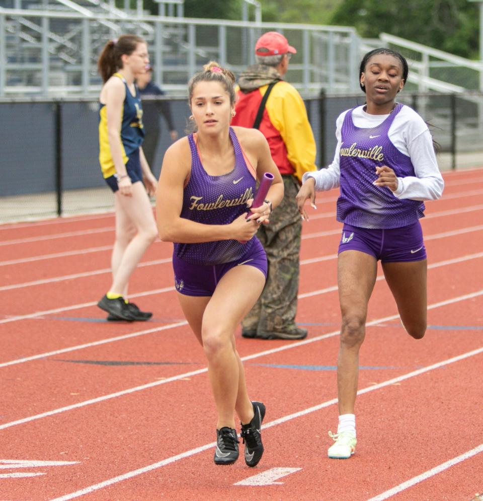 Fowlerville's Sarah Litz, left, runs the final leg of the 1,600-meter relay after taking the baton from Princess Nzaou-Pambou in the CAAC Red track and field meet at Lansing Eastern Wednesday, May 25, 2022.