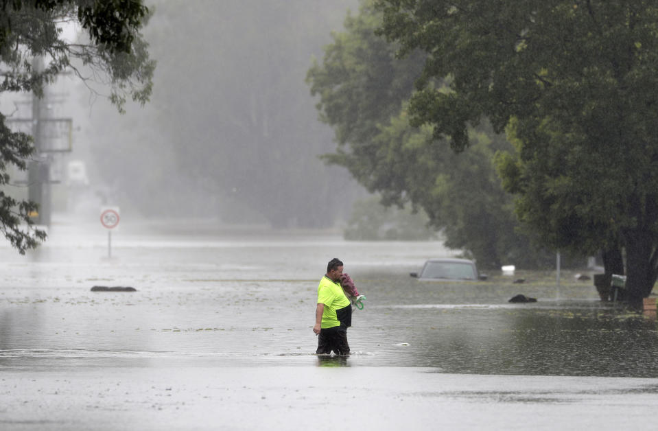 A man walks across a flooded street in Windsor, northwest of Sydney, New South Wales, Australia, Tuesday, March 23, 2021. Hundreds of people have been rescued from floodwaters that have isolated dozens of towns in Australia's most populous state New South Wales and forced thousands to evacuate their homes as record rain continues to inundate the country's east coast. (AP Photo/Rick Rycroft)