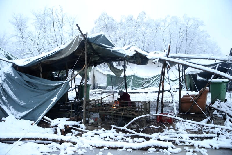 A migrant is seen next to a fire in a snow covered makeshift forest camp near Croatian border in Bihac