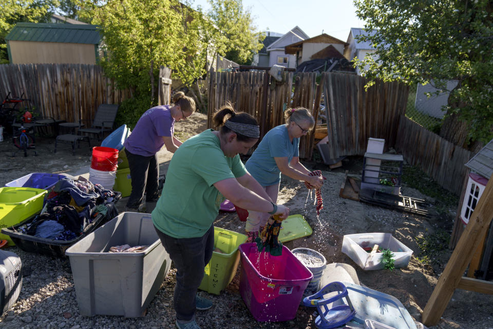 Kirstyn Brown, left, cleans out damaged clothing from her flooded home with the help of her mother, Cheryl Pruitt, right, and her sister-in-law, Randi Pruitt, in Red Lodge, Mont., Wednesday, June 15, 2022. On Wednesday, residents in Red Lodge, a gateway town to Yellowstone Park's northern end, used shovels, wheelbarrows and a pump to clear thick mud and debris from flooded homes along the banks of Rock Creek. (AP Photo/David Goldman)