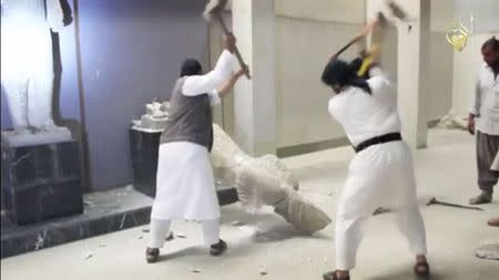 Men use sledgehammers on a toppled statue in a museum at a location said to be Mosul in this still image taken from an undated video. REUTERS/Social media Web site via Reuters TV