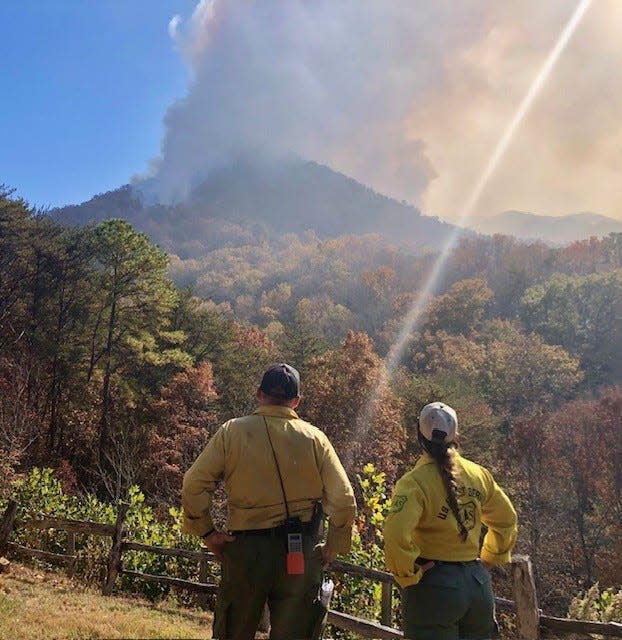 Two crew members stand looking at smoke coming from a wildfire, which spans thousands of acres in the Nantahala National Forest.