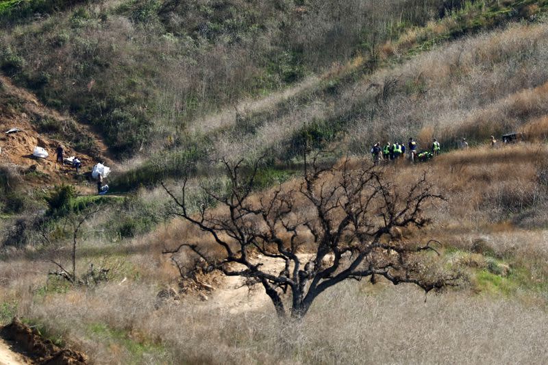 Personnel collect debris while working with NTSB investigators, right, at the helicopter crash site of NBA star Kobe Bryant in Calabasas, California