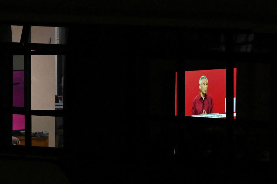A television screen (R) seen through the window of a residential apartment, shows a live broadcast of Singapore's Prime Minister Lee Hsien Loong delivering his National Day Rally speech in Singapore on August 21, 2022.<span class="copyright">ROSLAN RAHMAN/AFP via Getty Images</span>