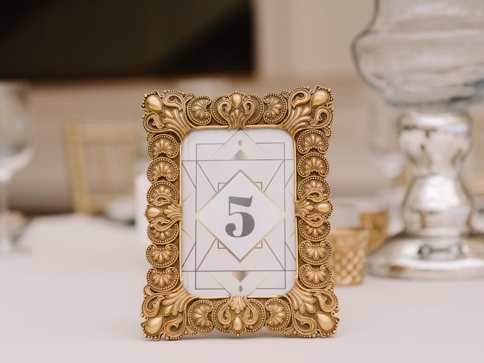 Gold frame with paper with "5" on it on table with glasses and white tablecloth
