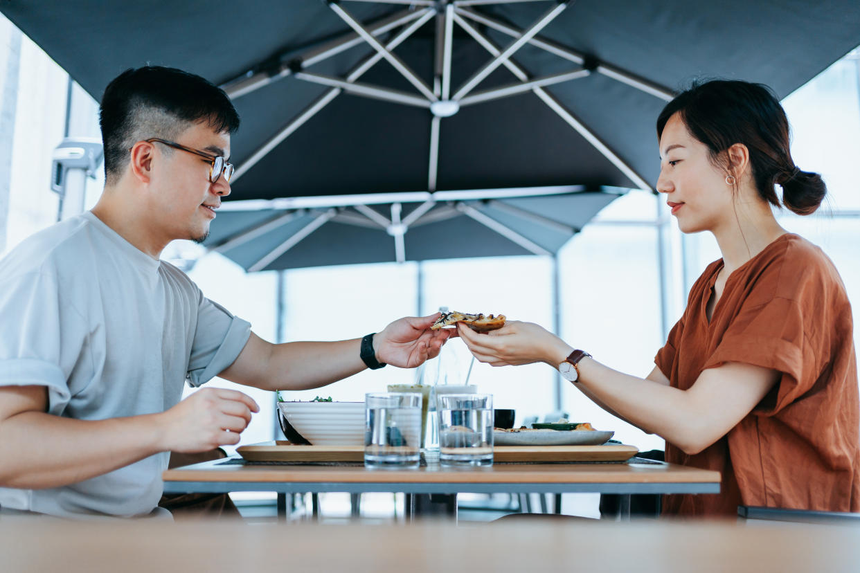 Young Asian couple enjoying a lunch date in an outdoor restaurant, sharing and eating freshly served pizza. Having a relaxing afternoon. Eating out lifestyle