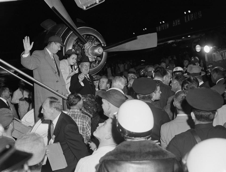 A man stands in front of airplane engine while a crowd below surrounds him.