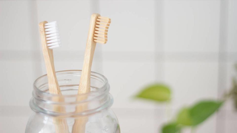 Two wooden manual toothbrushes in a glass holder