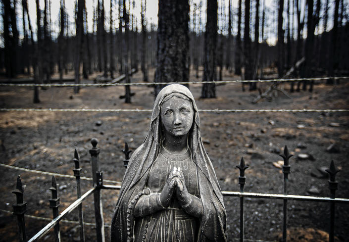 Blackened tombstones and statues stand at the Rociada Cemetery after fire tore through the area in the evacuation area near Mora, N.M., on Wednesday, May 4, 2022, where firefighters have been battling the Hermit's Peak and Calf Canyon fire for weeks. Many residents have resisted the evacuation orders opting to stay and protect their homes to face nature's fury. Weather conditions described as potentially historic are on tap for New Mexico on Saturday, May 7 and over the next several days as the largest fire burning in the U.S. chews through more tinder-dry mountainsides. (Jim Weber/Santa Fe New Mexican via AP)