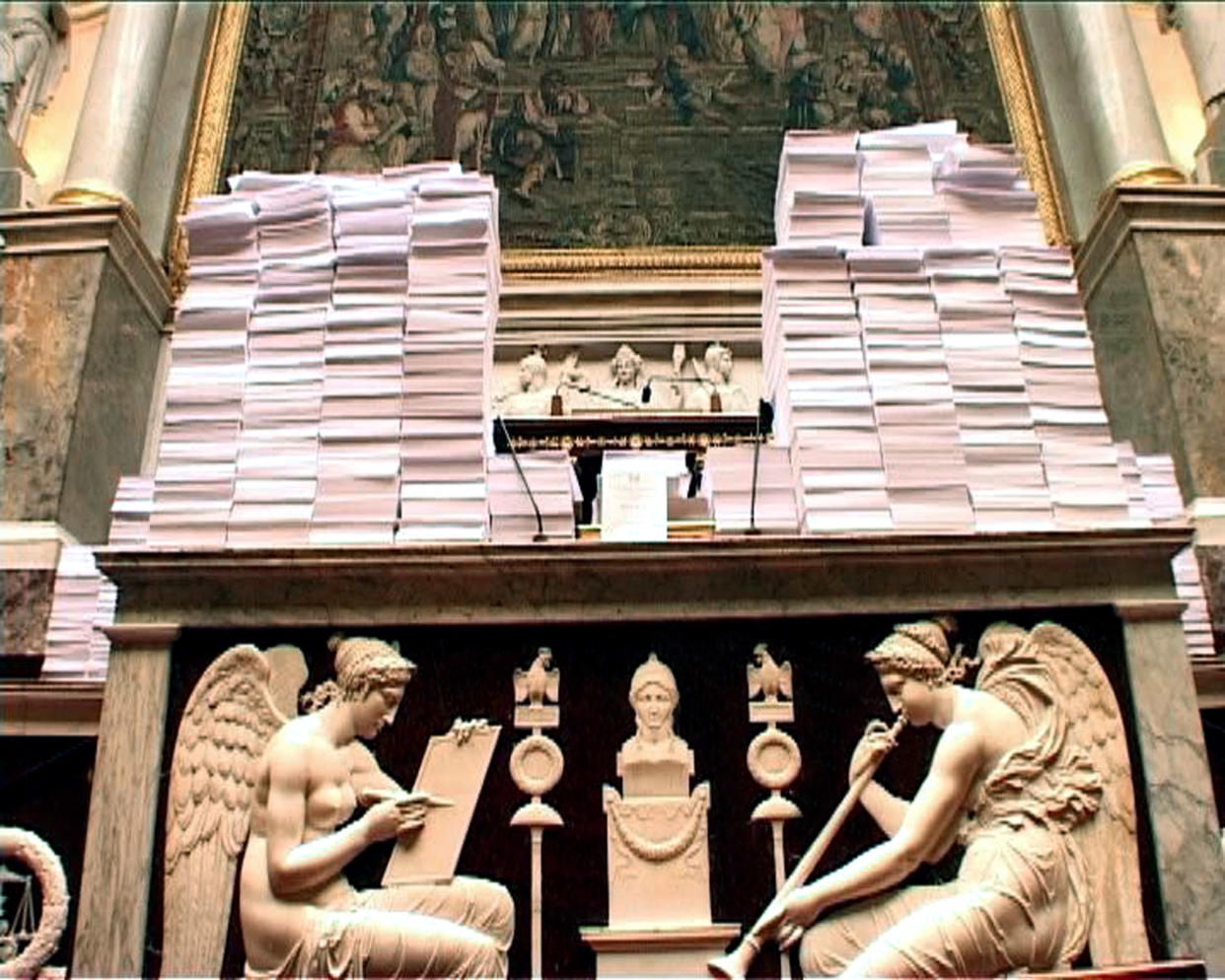 Capture d'écran de télévision prise le 05 septembre 2006 à l'Assemblée Nationale à Paris, montrant des piles de papier symbolisant les dizaines de milliers d'amendements déposés par l'opposition sur le projet de loi de fusion GDF-Suez posées sur le bureau du président de l'Assemblée nationale Jean-Louis Debré (Photo by AFP)