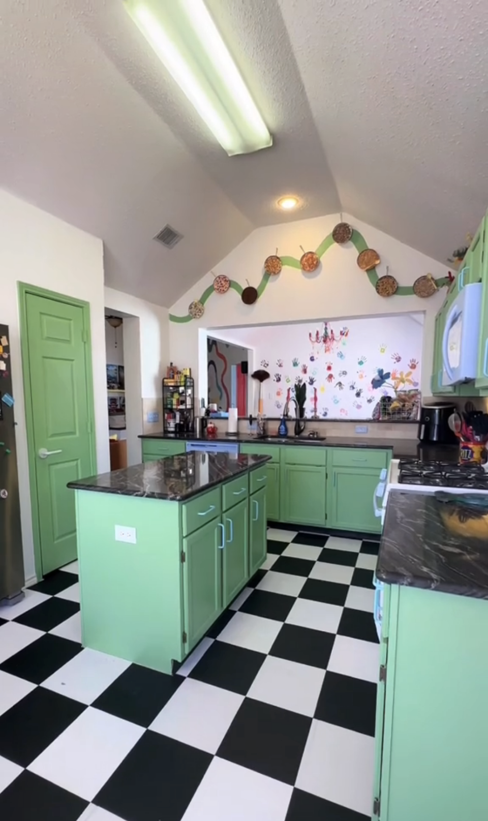 A kitchen with checkered floor, green cabinets, and various decorative items on walls and shelves