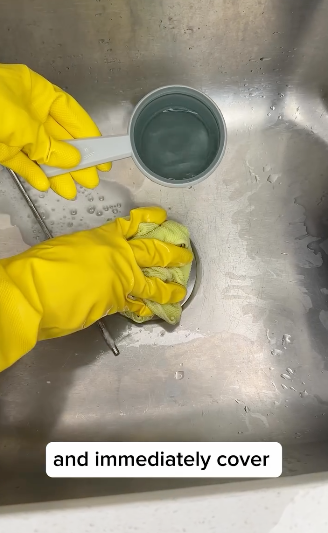 Hands wearing yellow gloves mix a substance in a cup placed in a sink with text "and immediately cover"
