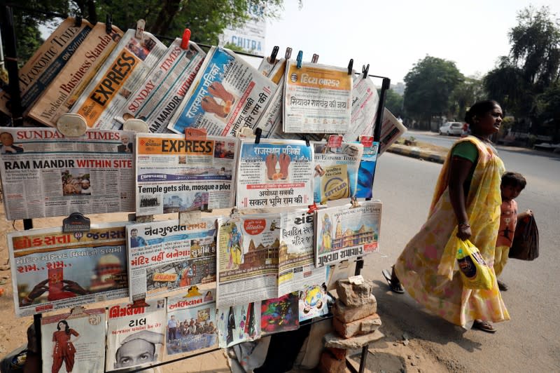 A woman with her son walks past newspapers hanging at a stall with the headlines about Supreme Court's verdict on a disputed religious site in Ayodhya, in Ahmedabad