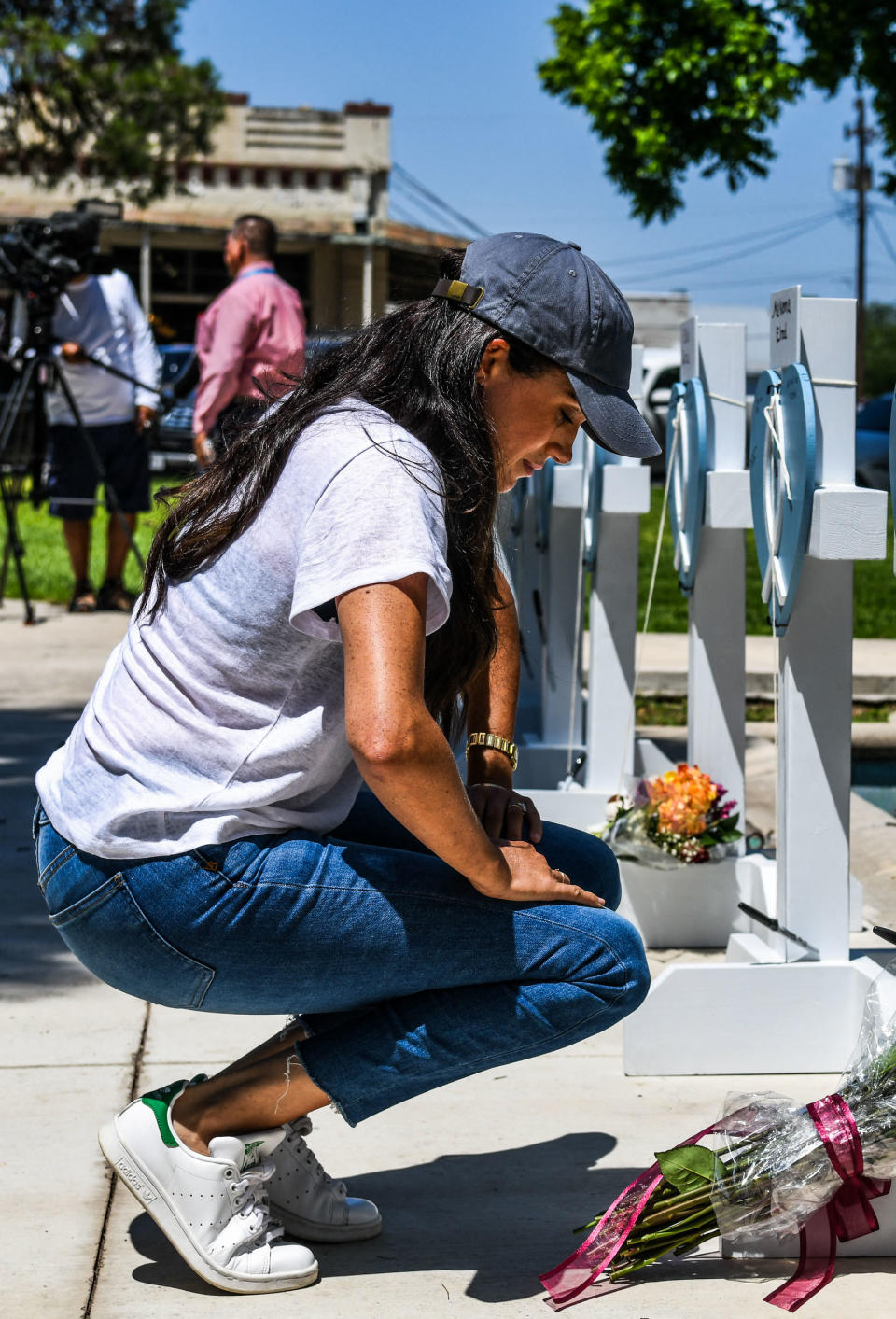 Meghan Markle crouches down to pay her respects to the school shooting victims, she's wearing jeans, white t shirt and black cap