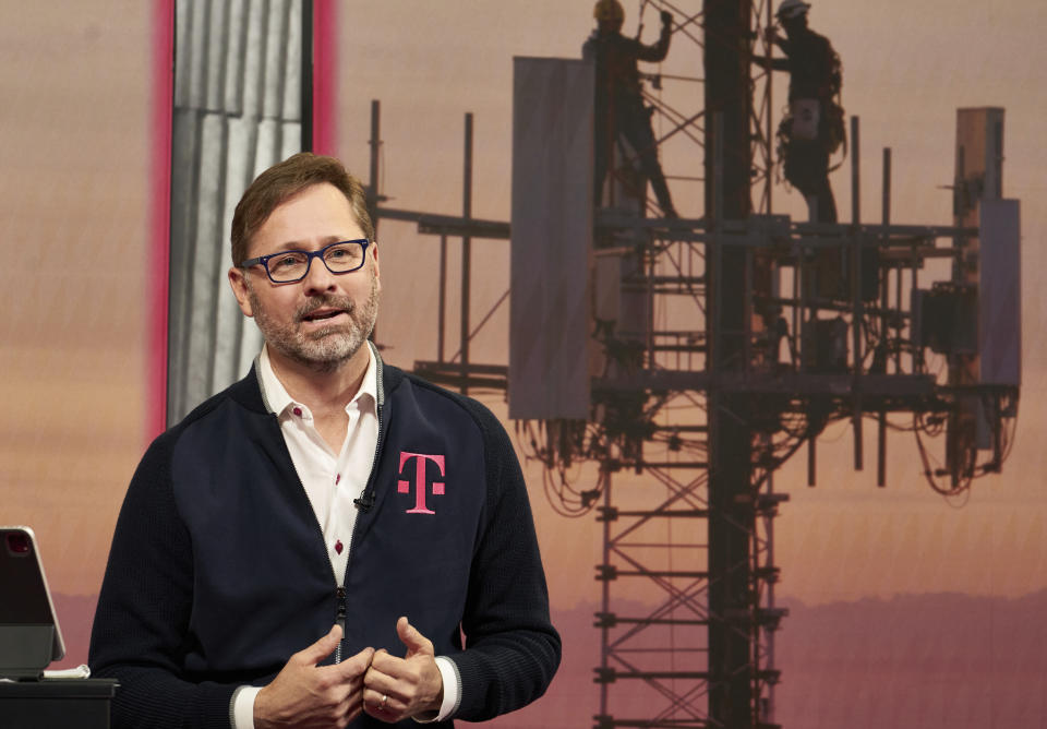 T-Mobile CEO Mike Sievert is shown presenting at the company's analyst day with an image of telecom workers in the background.