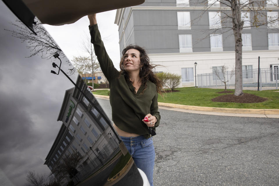 Kelsea Mensh, 22, puts her bag inside her car as she leaves a Holiday Inn Express in Dumfries, Va., Wednesday April 1, 2020, on her last day of a two week quarantine there following her evacuation from the Peace Corps in the Dominican Republic. The Peace Corps put Mensh up in a hotel in her hometown to self-isolate so that she wouldn't cause any risk to her mother, who is a cancer survivor and has viral induced asthma. (AP Photo/Jacquelyn Martin)