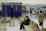 A passenger rests near arrival information screens for international flights at the Narita International Airport in Narita, east of Tokyo, Thursday, Dec. 2, 2021. Going further than many other countries in trying to contain the virus, Japan has banned foreign visitors and asked international airlines to stop taking new reservations for all flights arriving in the country until the end of December. (AP Photo/Hiro Komae)