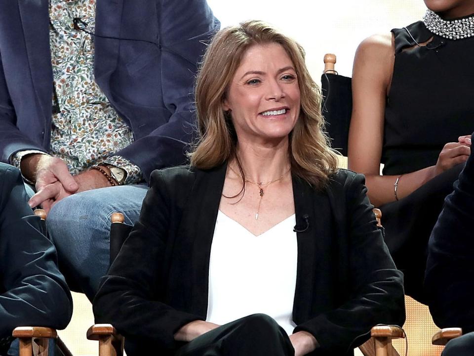 Gillian Vigman sits in a chair as part of a panel and wears a black suit and white shirt