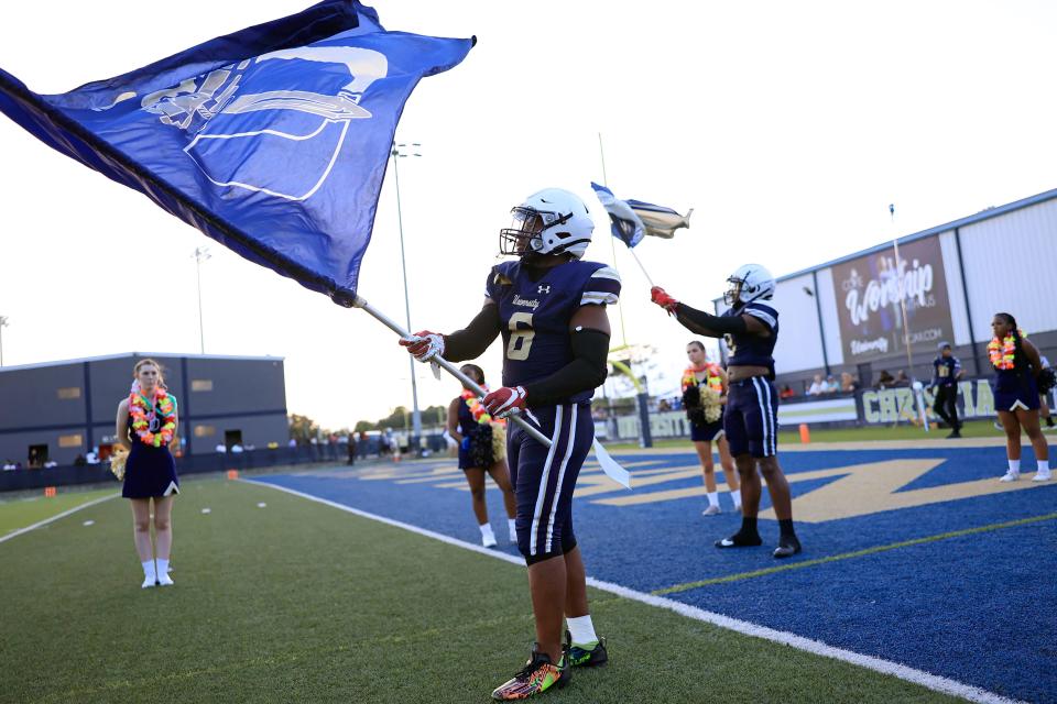 University Christian's Ethan Young (6) waves the school flag with teammate Isaac Colwell (3), right, before a regular season high school football matchup Friday, Aug. 25, 2023 at University Christian School in Jacksonville, Fla.