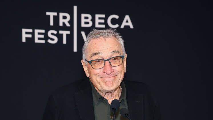 robert de niro smiling as he prepares to speak behind a podium microphone