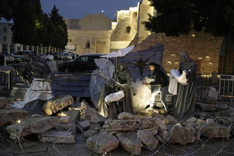 Un hombre decora una escena de Navidad, en Belén, con escombros que simbolizan la destrucción en Gaza y sábanas blancas por las víctimas