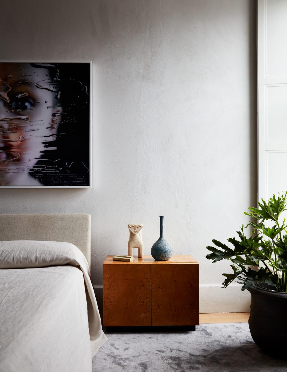 Under the Marilyn Minter portrait, the Milo Baughman bedside table holds an Italian vase and a 1970s limestone lamp by the French designer Alfred Tormos, from Glen Dooley Antiques.