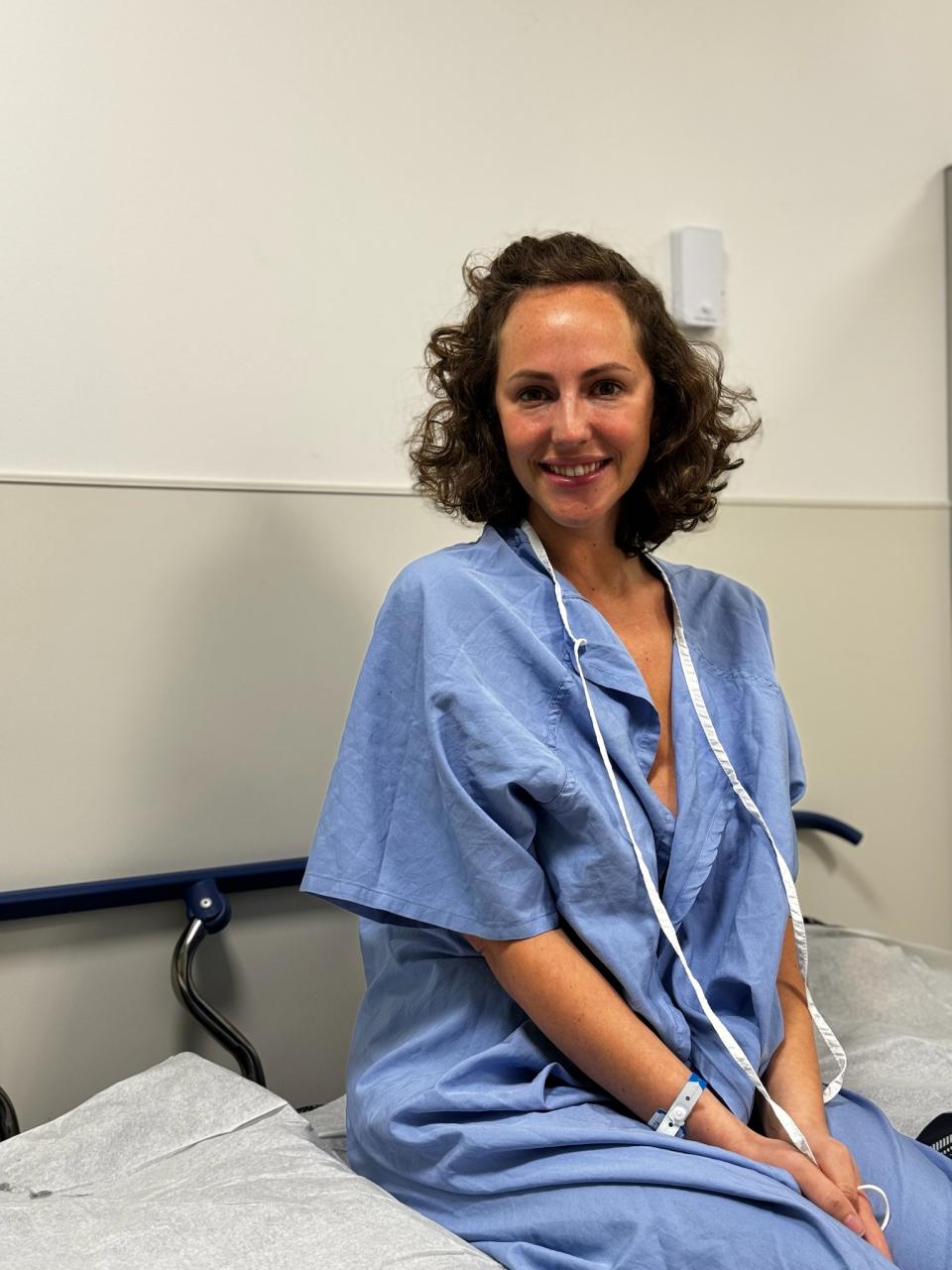 Robyn Goldman sits on a bed while wearing a blue hospital gown. (Photo provided by Robyn Goldman)