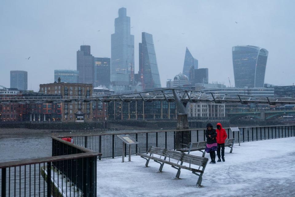 People walk on the south bank of the river Thames, in London during a snow shower in Feb 2021 (PA)