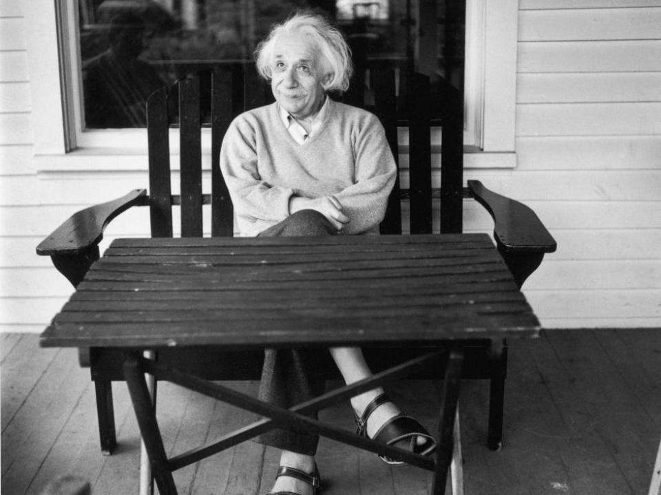 Albert Einstein sits in a chair behind a wooden table on his porch at home in Princeton, New Jersey.