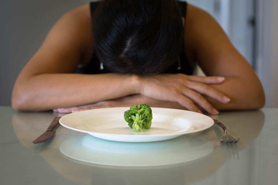 A woman sitting in front of a plate with a small portion of vegatables, looking miserable and hungry.