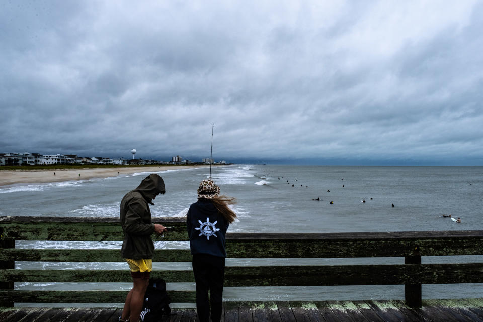 People look at surfers riding the waves in Wilmington, North Carolina on Saturday.