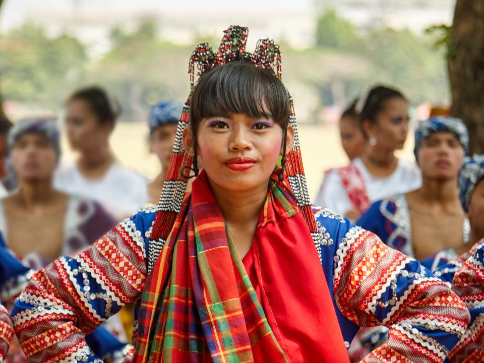 A dancer standing in front of a group of people with her hands on her hips while wearing an ornate-looking dress.