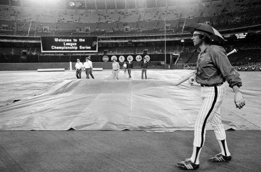 Phillie’ Jay Johnstone wears an umbrella hat as grounds crew pull tarp onto field at Veteran Stadium, Saturday, Oct. 8, 1977 in Philadelphia. Rain delayed some of pregame workouts before Phillies play Los Angeles Dodgers at National League playoffs. (AP Photo)