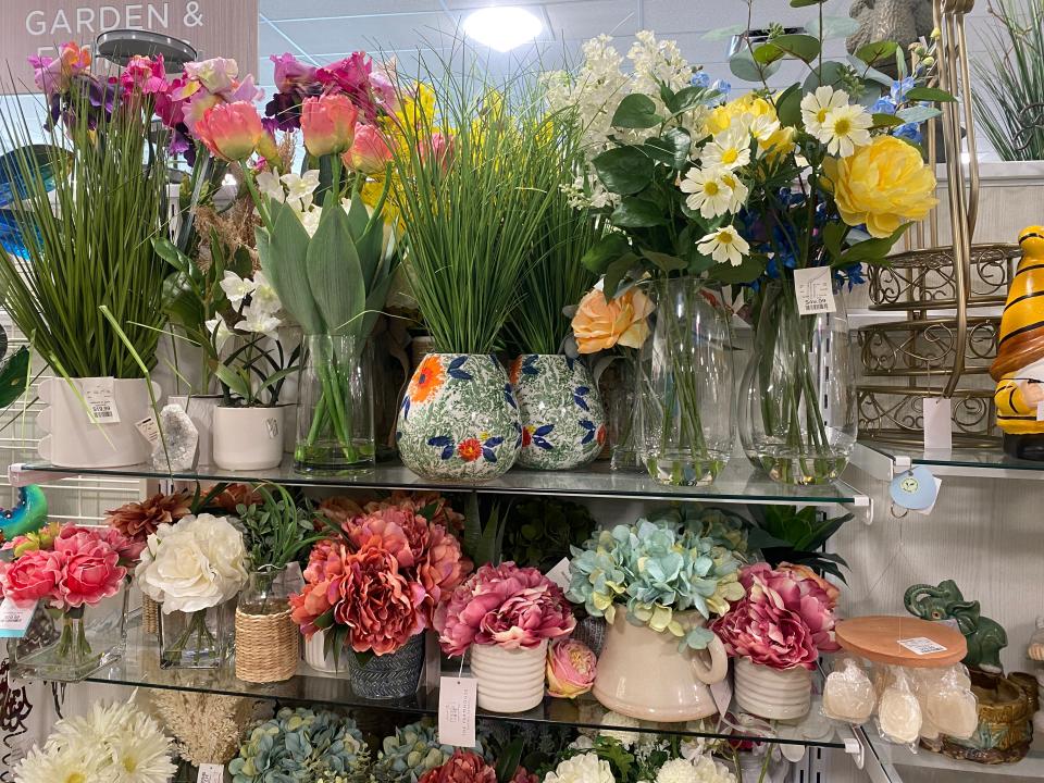 Glass shelves with faux plants and flowers in a variety of vases in a homegoods