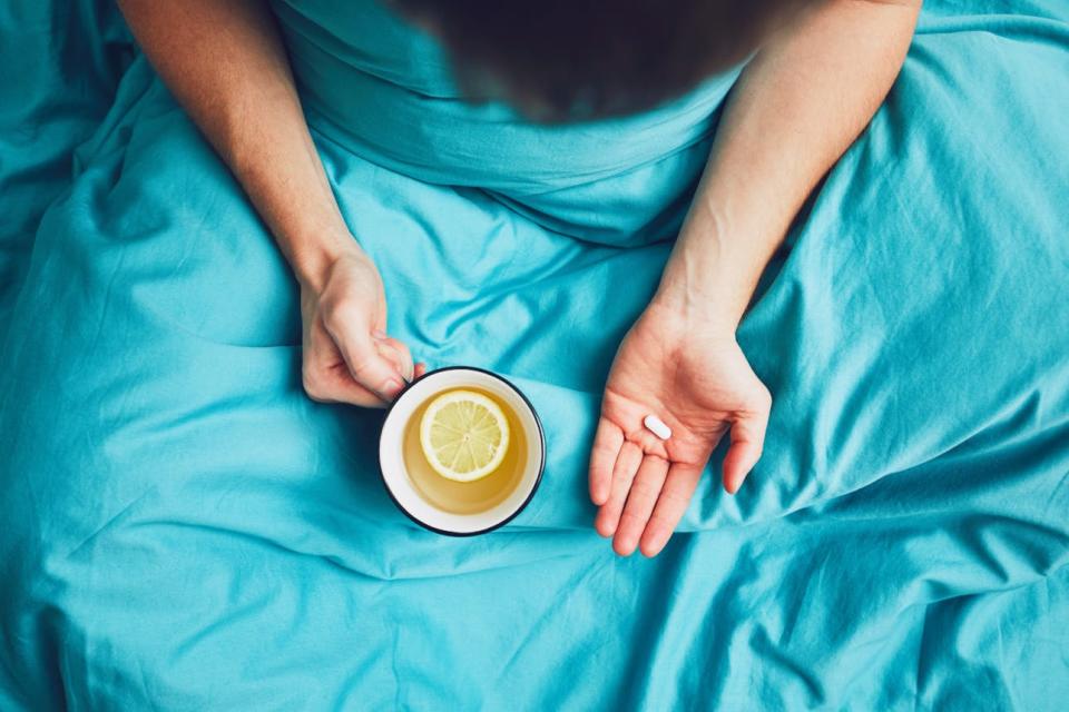 A person holds a pill and a mug of tea with a slice of lemon